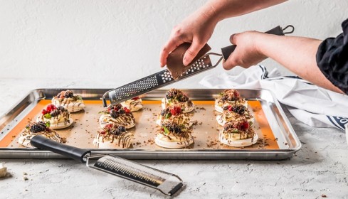 Commercial baker using a fine grater to finish plated desserts on a professional baking tray